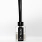 A clear bottle containing natural diffuser scented with rose and oud, has a cwtch label on the front and 7 black diffuser reeds